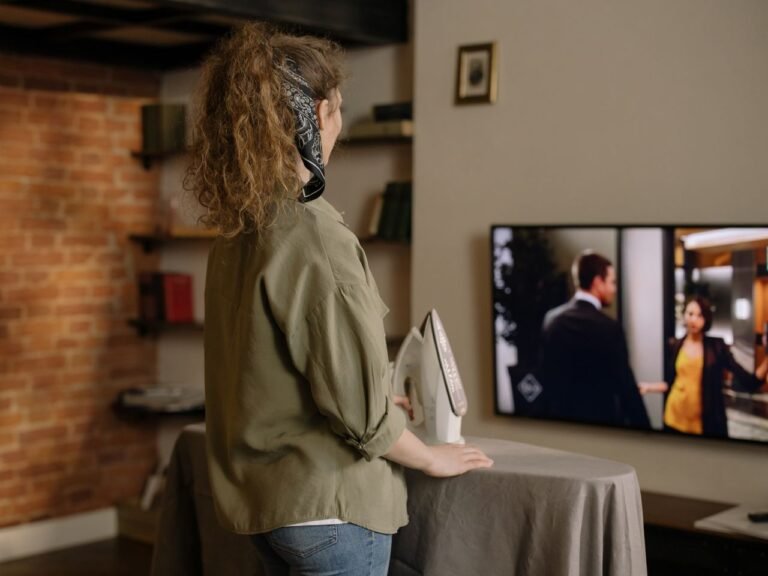 A woman ironing while watching TV in a cozy brick-walled living room.